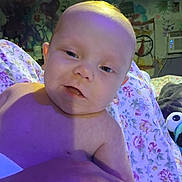 Jerald is registered to the contest to win money with this photo: baby, child, face, close_up, indoor, blanket, floral_pattern, lighting, purple_light, yellow_light, toy, colorful_background, expression, skin, young_child, portrait, person, hand, bald, cute