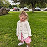 child, toddler, girl, portrait, outdoor, park, grass, lawn, smiling, playful, standing, cardigan, pink_shorts, sneakers, ponytail, trees, boulders, parked_cars, cloudy_sky, nature