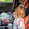 child, toddler, car, car_interior, dog, pet, seated, back_view, long_hair, blanket, snack, drink, cup, car_seat, seat_cover, road_trip, vehicle, indoor, family, colorful_clothing