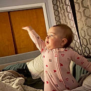 Finleigh Rae joined the competition — help win amazing prizes! baby, child, onesie, pink_clothing, heart_pattern, bedroom, blanket, pillow, curtains, wooden_door, infant, person, indoor, cute, sleepwear, smiling, playful, cozy, soft_light, furniture