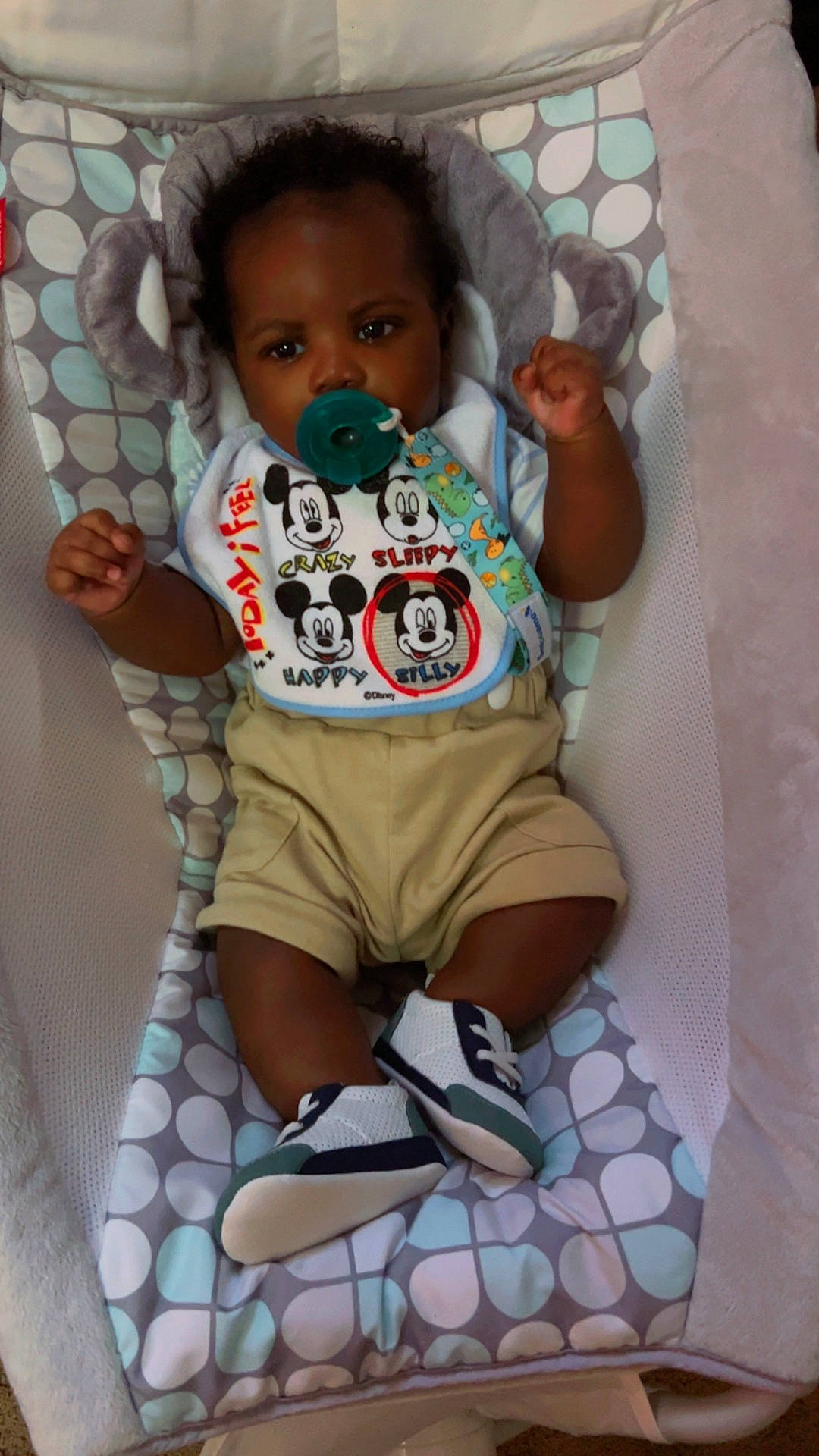 Damian joined the competition — help win amazing prizes! baby, baby_accessory, baby_seat, bib, child, clothing, cute, indoors, infant, mickey_mouse, moccasins, pacifier, patterned_cushion, person, portrait, relaxed, seated, small_shoes, sneakers, young_child