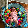 Ella Mae is registered to the contest to win money with this photo: baby, infant, playpen, colorful_balls, toy, floor, wooden_floor, romper, smiling, happy, child, indoor, playtime, cute, face, person, fabric, pattern, mesh, colorful