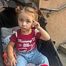blanket, building, child, girl, hair_ties, hand_gesture, handrail, heart_pattern, jeans, outdoor, photography, pigtails, portrait, red_shirt, serious_expression, sitting, slippers, stroller, toddler, walkway