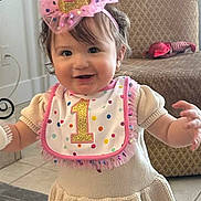Raylene joined the competition — help win amazing prizes! baby, child, birthday, party_hat, bib, cream_dress, indoor, standing, smiling, happy, floor, armchair, sock, pom_pom, knitted_clothing, celebration, cute, one_year_old, toddler, person