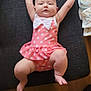baby, infant, swimsuit, polka_dot, pink, white_bow, cushion, diapers, indoor, child, cute, chubby, lying_down, arms_up, floor, footwear, person, portrait, soft_lighting, home
