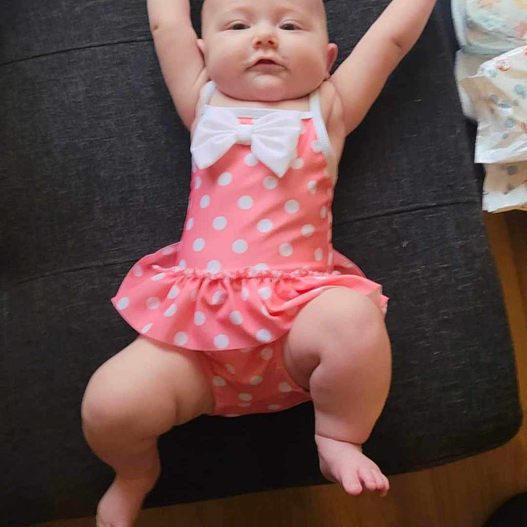 Deianira joined the competition — help win amazing prizes! arms_up, baby, child, chubby, cushion, cute, diapers, floor, footwear, home, indoor, infant, lying_down, person, pink, polka_dot, portrait, soft_lighting, swimsuit, white_bow
