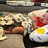 baby, kitten, blanket, pillow, dinosaur_pattern, red_clothing, cute, indoor, sleeping_cat, infant, child, resting, cozy, pet, animal, soft_toys, playpen, comfort, face, legs