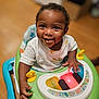 baby, child, walker, toy, light, smile, happy, food_stains, indoor, floor, clothing, playtime, cute, infant, person, furniture, colorful, hand, face, young