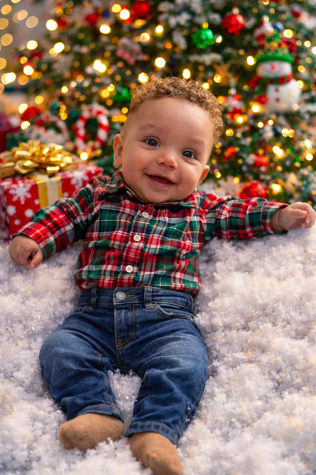 Jeremiah joined the competition — help win amazing prizes! baby, child, smiling, plaid_shirt, jeans, christmas_tree, holiday_lights, snow, gift_box, festive, curly_hair, indoors, cute, happy, decorations, seasonal, sitting, portrait, celebration, warmth