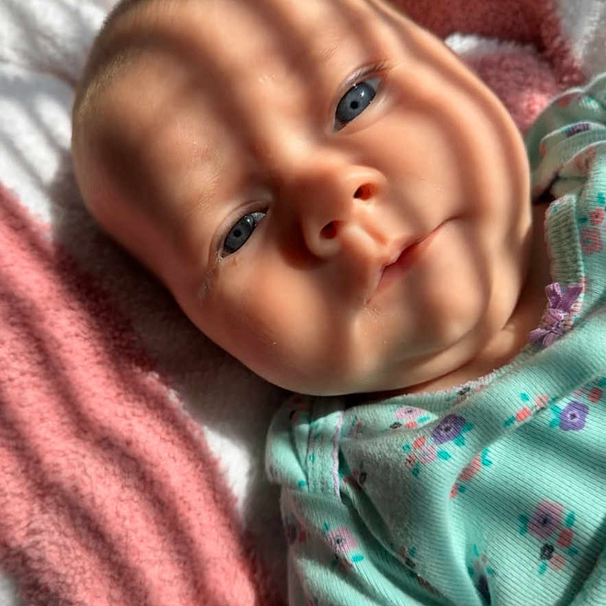 Vaeda joined the competition — help win amazing prizes! baby, blanket, blue_eyes, child, closeup, clothing, cute, face, floral_pattern, head, indoors, infant, lying_down, newborn, portrait, skin, sleepy, soft_texture, striped_shadow, warm_light