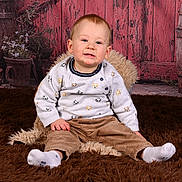 Charlie participe au concours pour gagner de l'argent avec cette photo : baby, brown_pants, casual_clothing, child, cozy, cute, floor, fluffy_rug, indoor, plant_pots, portrait, rustic, sitting, smiling, studio_photo, sweater, toddler, white_socks, wooden_backdrop, young_child