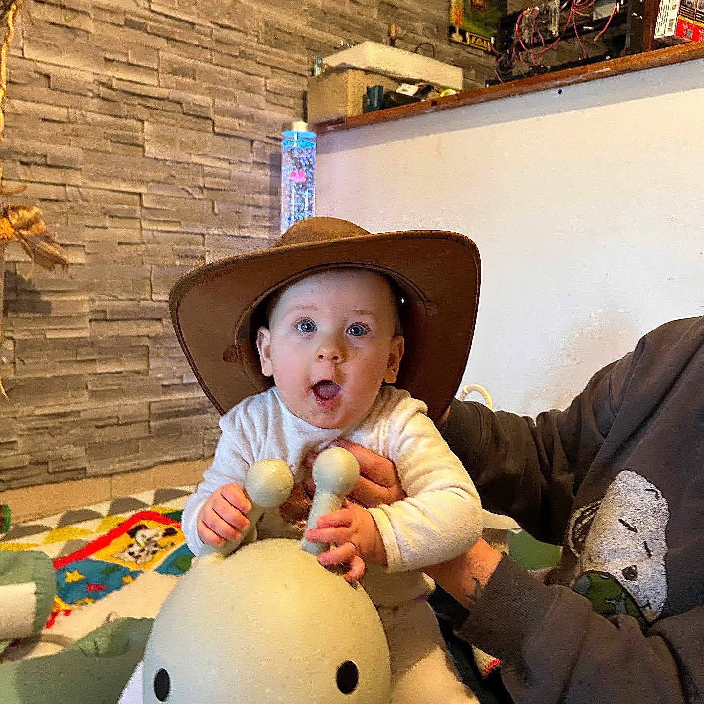 Charlie participe au concours pour gagner de l'argent avec cette photo : baby, child, clothing, colorful, cowboy_hat, cute, face, floor, hand, headwear, indoor, person, play_mat, sitting, snail_toy, supporting_hand, surprised_expression, toy, wall, young_child