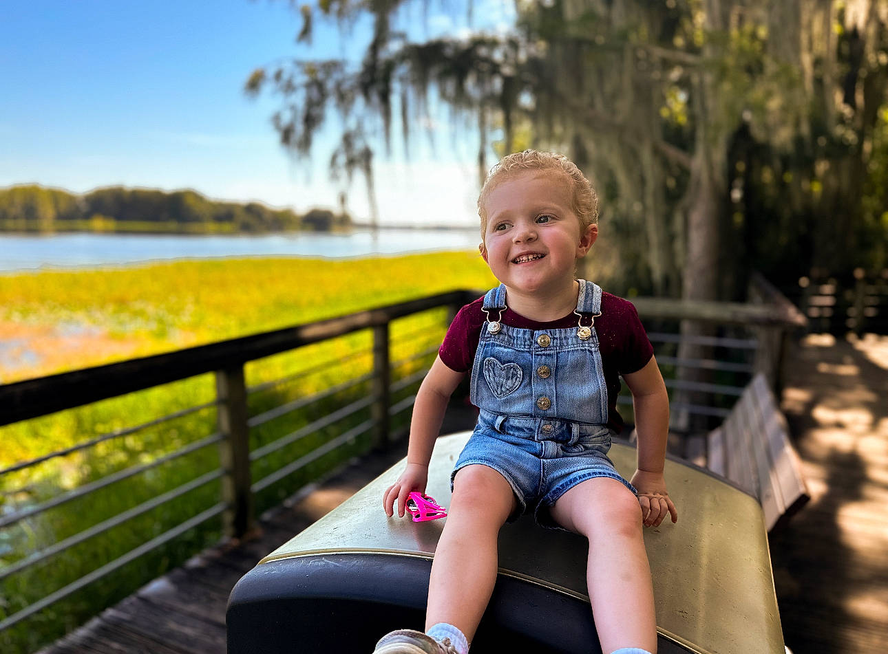Maisyn is registered to the contest to win money with this photo: child, fence, flash_photography, fun, grass, happy, joy, lake, leisure, morning, people_in_nature, person, plant, recreation, shorts, sky, smile, summer, sunlight, t_shirt