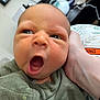 Liam is registered to the contest to win money with this photo: baby, newborn, yawning, close_up, infant, face, hand, clothing, green_outfit, person, indoor, expression, skin, head, human, portrait, cute, sleepy, small, child