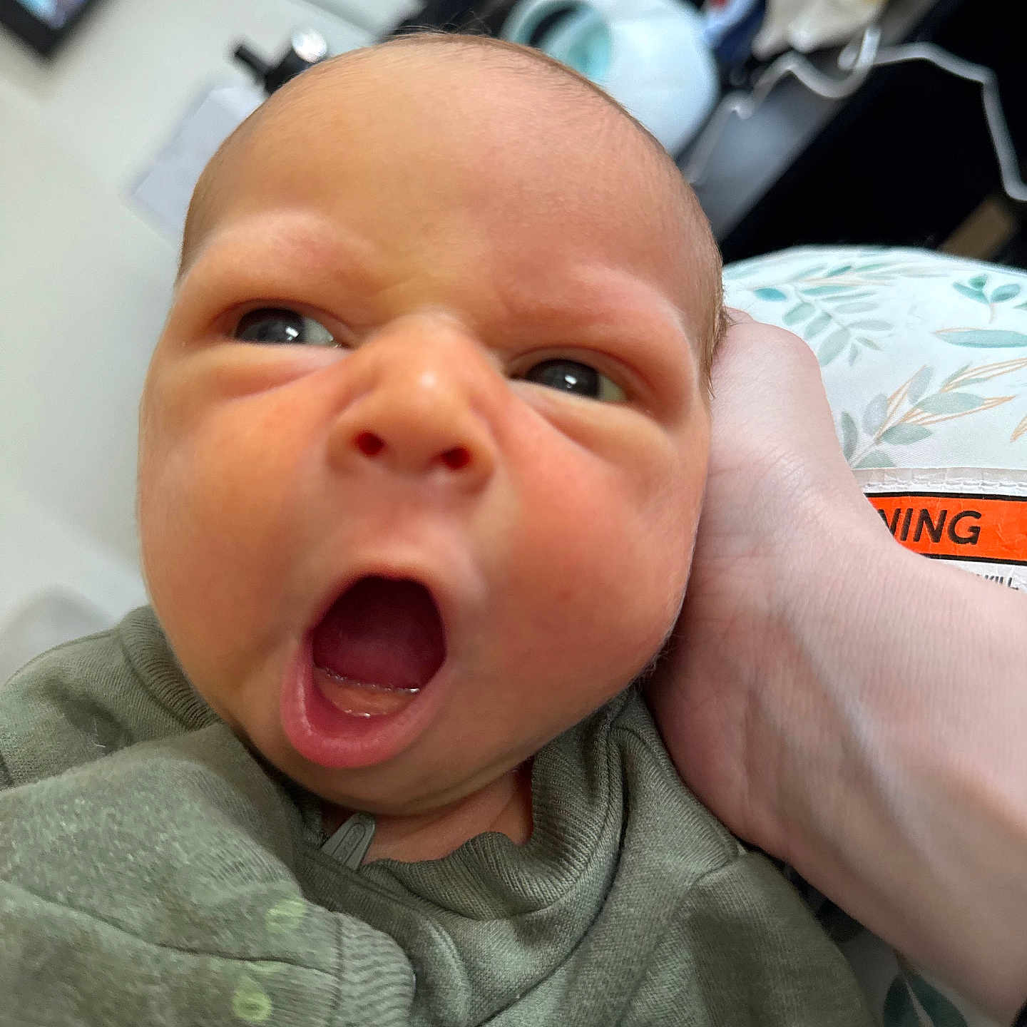 Liam is registered to the contest to win money with this photo: baby, child, close_up, clothing, cute, expression, face, green_outfit, hand, head, human, indoor, infant, newborn, person, portrait, skin, sleepy, small, yawning