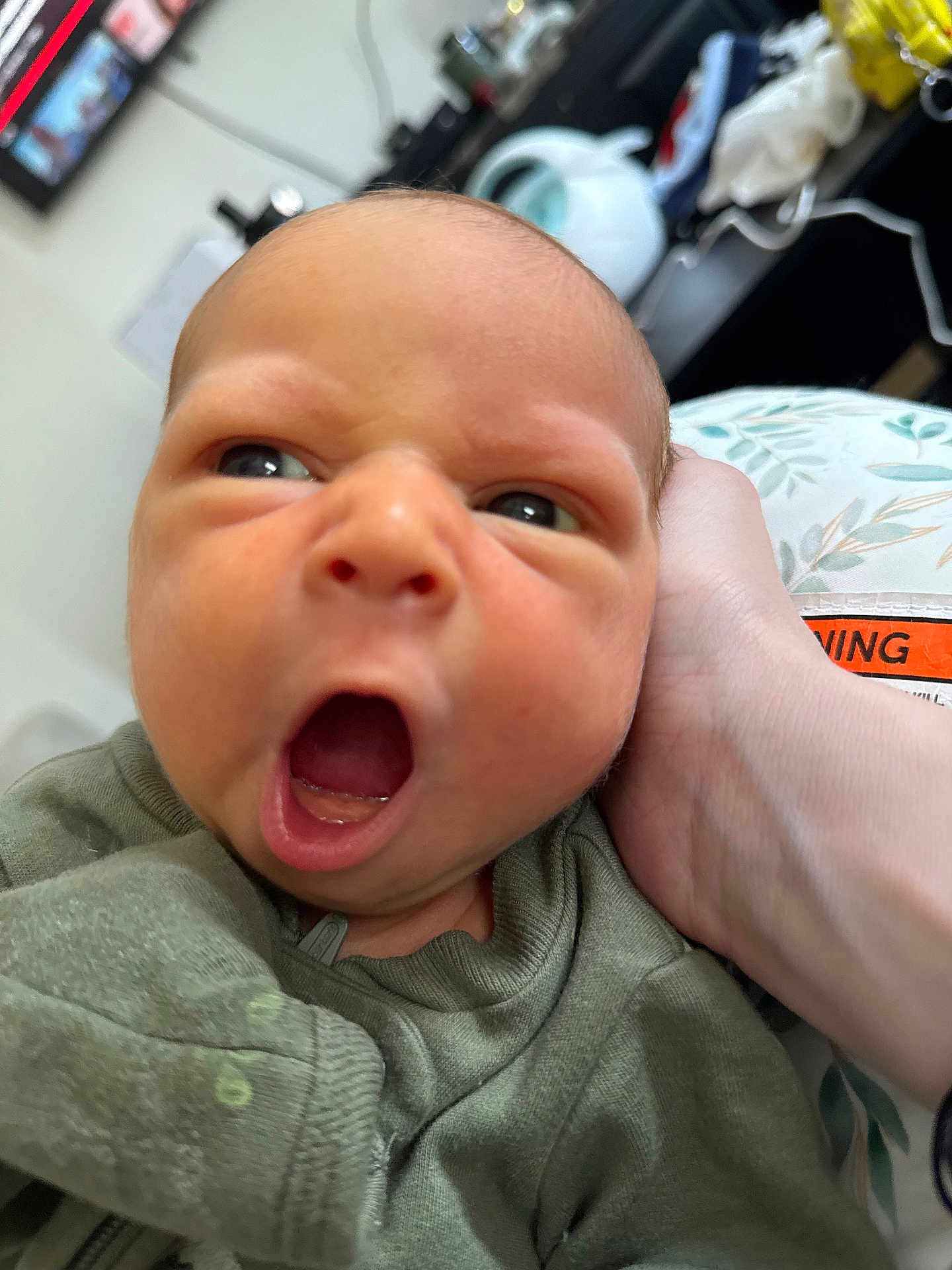 Liam is registered to the contest to win money with this photo: baby, newborn, yawning, close_up, infant, face, hand, clothing, green_outfit, person, indoor, expression, skin, head, human, portrait, cute, sleepy, small, child
