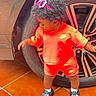 child, toddler, curly_hair, sunglasses, orange_outfit, sportswear, nike, shorts, shirt, shoes, clogs, socks, standing, car, wheel, tire, vehicle, outdoor, tile_floor, portrait