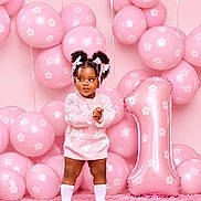 Jazlynn joined the competition — help win amazing prizes! backdrop, balloons, birthday, bows, braids, carpet, celebration, child, floral_pattern, indoor, number_one, party, photography, pink, portrait, smiling, socks, standing, sweater, toddler