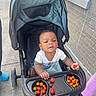 Emmanuel is registered to the contest to win money with this photo: baby, child, infant, stroller, sitting, outdoor, sidewalk, tomatoes, cherry_tomatoes, vegetables, food, snack, white_shirt, blanket, baby_carriage, curious, portrait, brick_wall, daylight, family