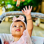 Pahal joined the competition — help win amazing prizes! baby, child, infant, pink_dress, headband, bow, hand, bracelet, stroller, toy, wooden_toy, outdoor, blurred_background, curious, looking_up, face, portrait, candid, soft_light, cute