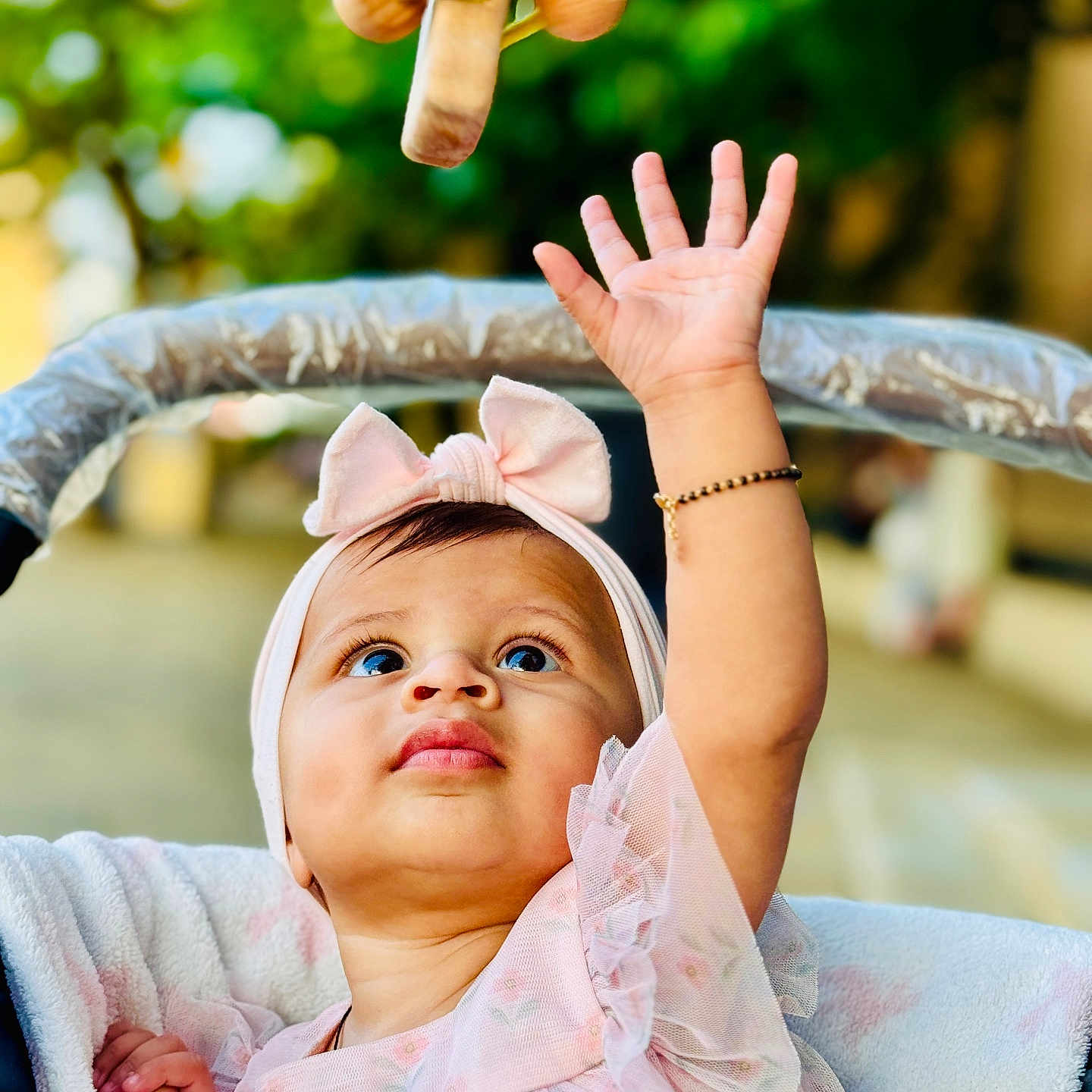 Pahal joined the competition — help win amazing prizes! baby, blurred_background, bow, bracelet, candid, child, curious, cute, face, hand, headband, infant, looking_up, outdoor, pink_dress, portrait, soft_light, stroller, toy, wooden_toy