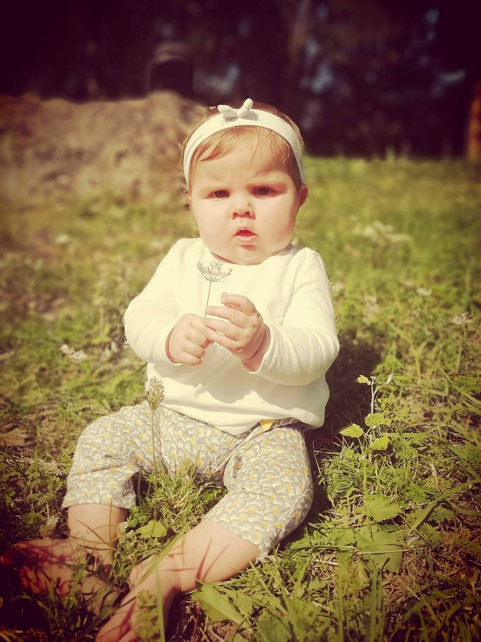 Heloise participe au concours pour gagner de l'argent avec cette photo : baby, child, dress, eye, grass, grass_family, green, happy, leaf, people, people_in_nature, person, photograph, photography, plant, portrait, sitting, smile, sunlight, toddler