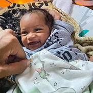 Nyzaiah is registered to the contest to win money with this photo: baby, smiling, blanket, hand, indoor, cozy, infant, clothing, face, person, cute, warm_light, toddler, expression, comfort, furniture, soft, portrait, happy, playful