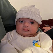 Rabab is registered to the contest to win money with this photo: baby, infant, hat, clothing, sleeve, face, eyes, person, portrait, indoor, hand, holding, cute, young, newborn, soft, warm, neutral_background, expression, closeup