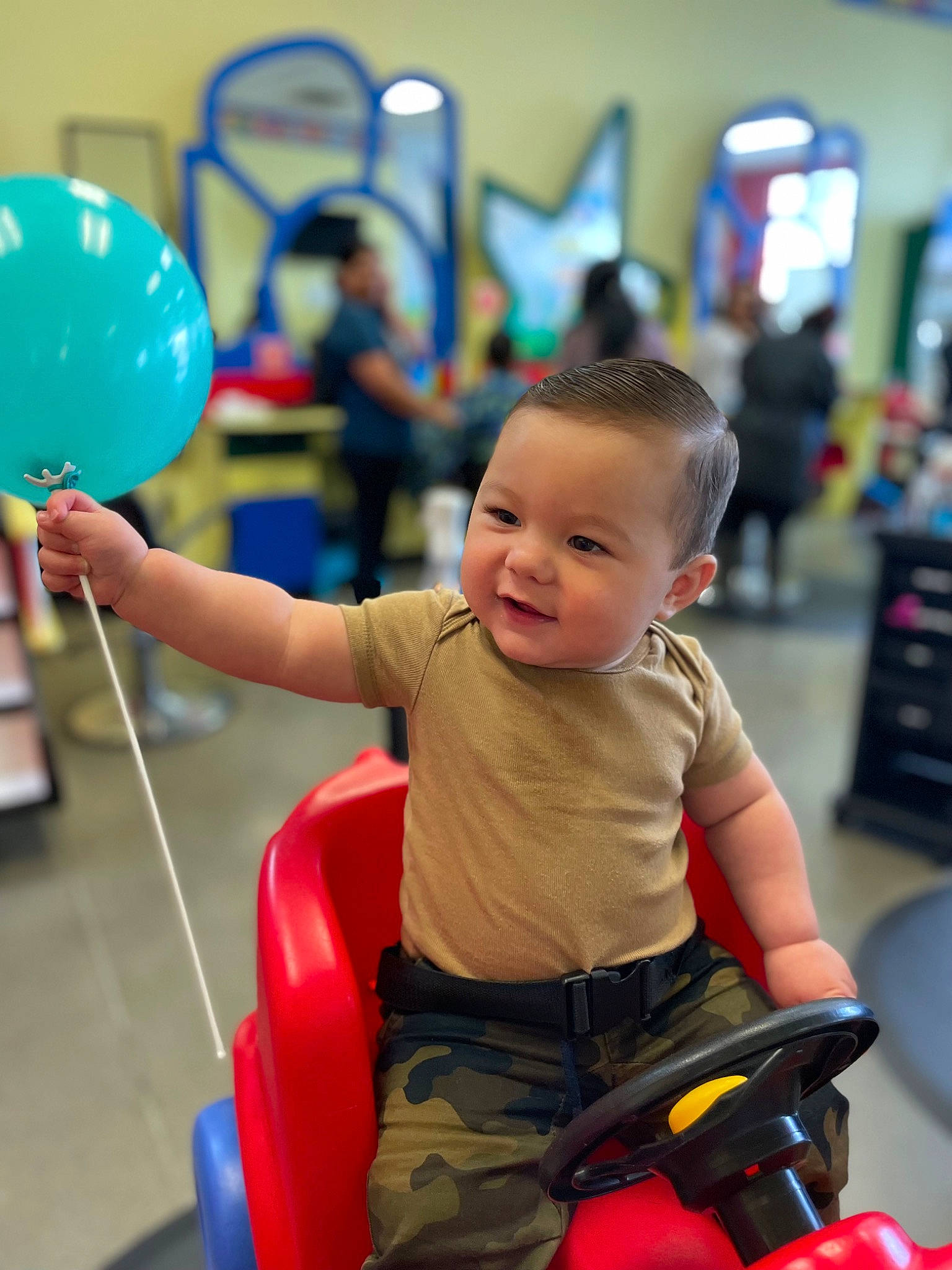 Brodie is registered to the contest to win money with this photo: baby, balloon, blue, child, electric_blue, event, flooring, fun, joy, leisure, party_supply, person, play, recreation, room, shorts, sitting, snapshot, t_shirt, toddler
