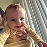 baby, child, infant, smiling, happy, portrait, close_up, indoor, window, blinds, sunlight, yellow_clothing, striped_outfit, adult_hand, caregiver, sitting, playful, face, home, photography