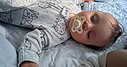 Connor is registered to the contest to win money with this photo: baby, sleeping, pacifier, infant, bed, blanket, quilt, pajamas, clothing, portrait, indoors, cozy, resting, face, closed_eyes, hand, arm, soft_lighting, nursery, peaceful