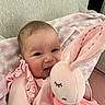 Ella is registered to the contest to win money with this photo: baby, infant, smiling, plush_toy, bunny, pink_clothing, couch, blanket, soft_toy, happy, child, portrait, indoors, cute, person, cozy, baby_girl, ruffles, fabric, comfort