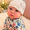 baby, child, infant, hat, floral_clothing, cute, rosy_cheeks, face, portrait, indoors, soft_lighting, bokeh, cozy, warm_colors, expression, sitting, fairy_lights, background_blur, headwear, person