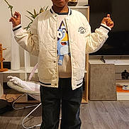 Mohamed a rejoint le concours — aidez-le/la à gagner de superbes lots ! child, boy, indoor, standing, jacket, cartoon_tshirt, sneakers, wood_floor, living_room, television, plant, baby_rocker, casual_clothing, smile, pose, home, furniture, floor, person, cute