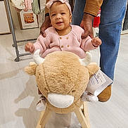 Fatima participe au concours pour gagner de l'argent avec cette photo : baby, child, adult, rocking_toy, plush_toy, indoor, clothing, pink_sweater, headband, smiling, supporting_hands, wooden_floor, jacket, jeans, footwear, hanger, clothes, toy, person, happy