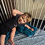 toddler, child, crib, blanket, bed, blue, white, zigzag_pattern, smiling, happy, hair, clothing, shorts, shirt, indoor, person, foot, hand, face, playful