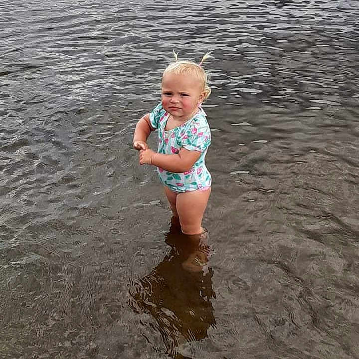 Elora is registered to the contest to win money with this photo: baby, beach, clothing, coast, face, head, lake, nature, outdoors, person, photography, portrait, rock, sea, shoreline, shorts, summer, swimwear, water, waterfront