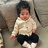 baby, child, infant, portrait, sitting, sofa, couch, cushions, cardigan, clothing, black_pants, white_socks, dark_hair, face, eyes, smiling, indoor, home, cozy, photography