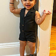 Vamika joined the competition — help win amazing prizes! toddler, child, smiling, standing, black_clothing, romper, sandals, hair_bow, bracelets, wooden_floor, wall, indoors, happy, cute, person, fashion, portrait, playful, young_child, feet