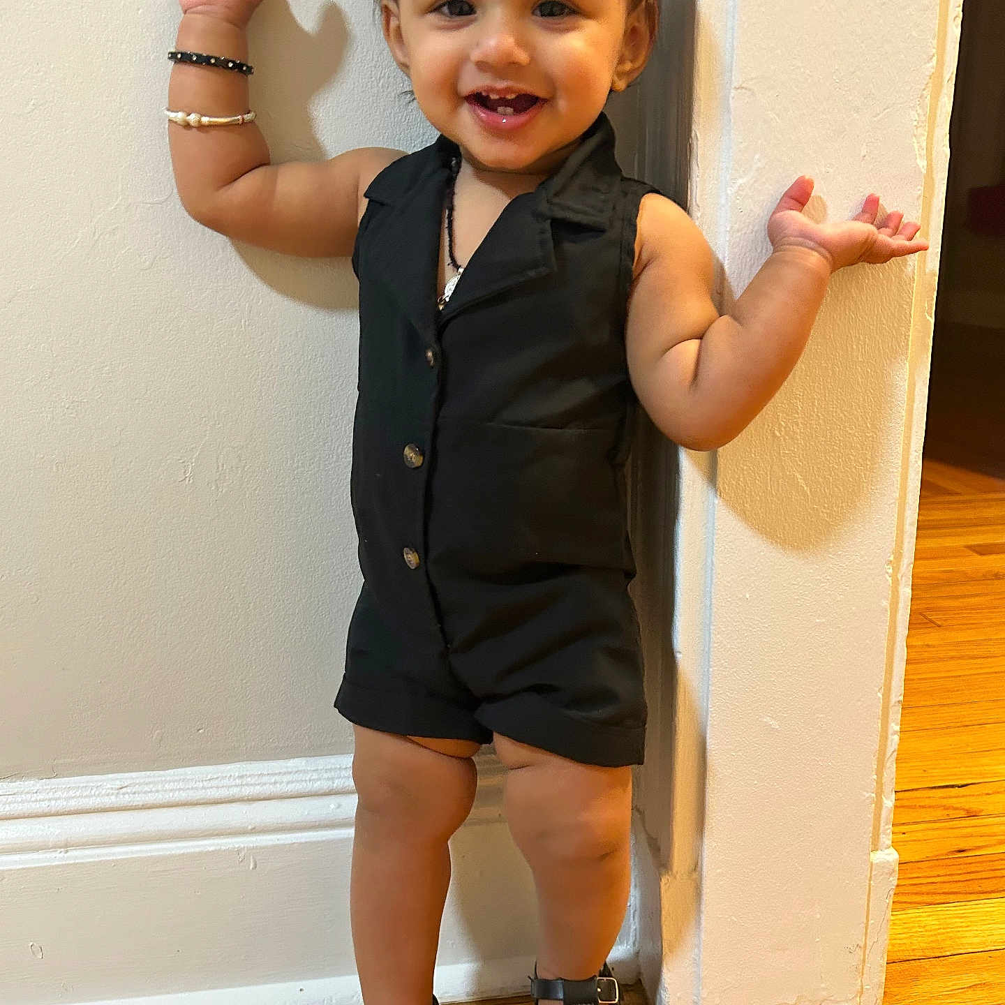 Vamika joined the competition — help win amazing prizes! black_clothing, bracelets, child, cute, fashion, feet, hair_bow, happy, indoors, person, playful, portrait, romper, sandals, smiling, standing, toddler, wall, wooden_floor, young_child