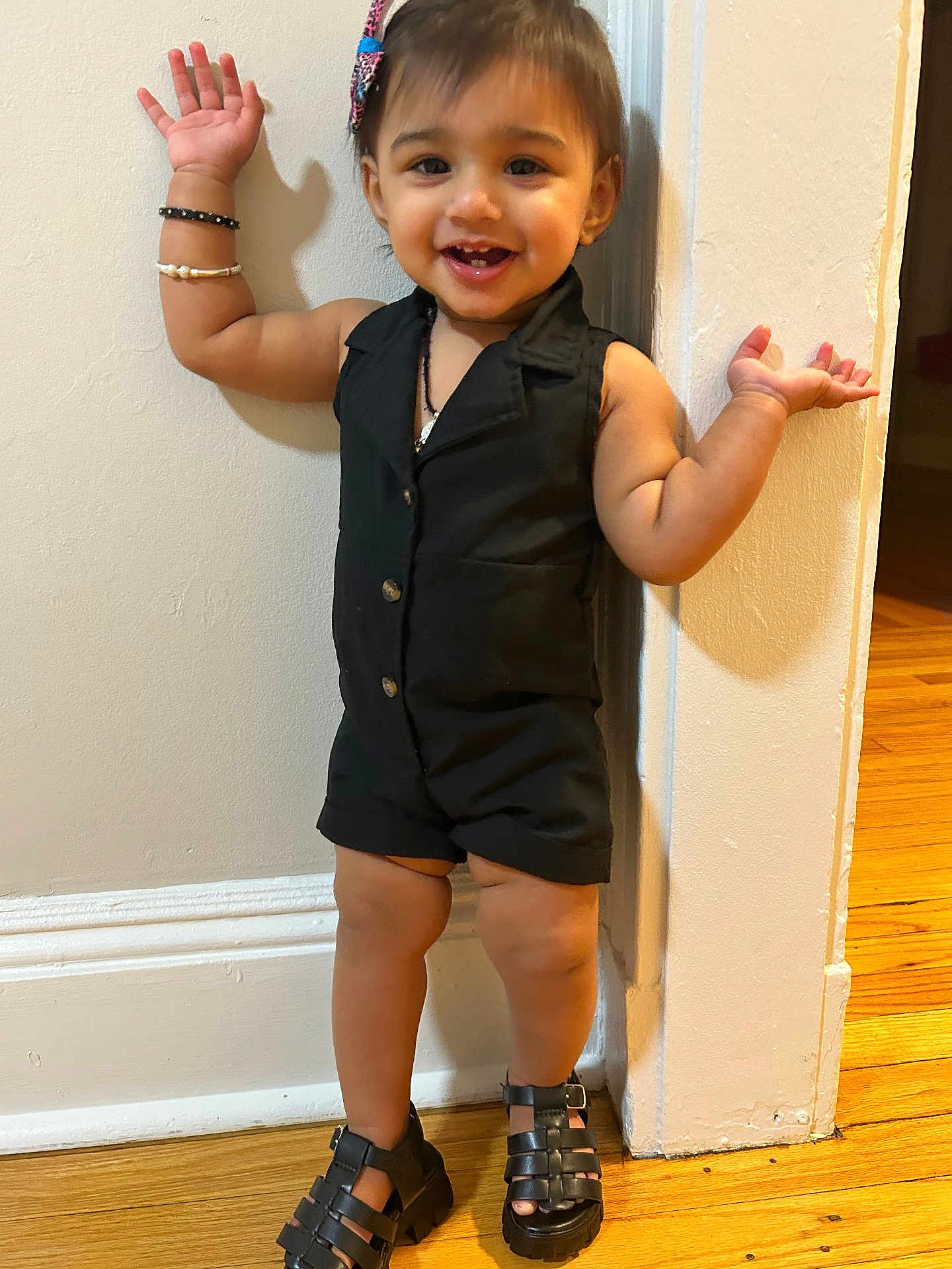 Vamika joined the competition — help win amazing prizes! toddler, child, smiling, standing, black_clothing, romper, sandals, hair_bow, bracelets, wooden_floor, wall, indoors, happy, cute, person, fashion, portrait, playful, young_child, feet