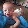 baby, diaper, blue_blanket, carpet, smiling, indoor, child, person, floor, toy, gaming_chair, happy, young_child, skin, head, arm, hand, face, candid, home