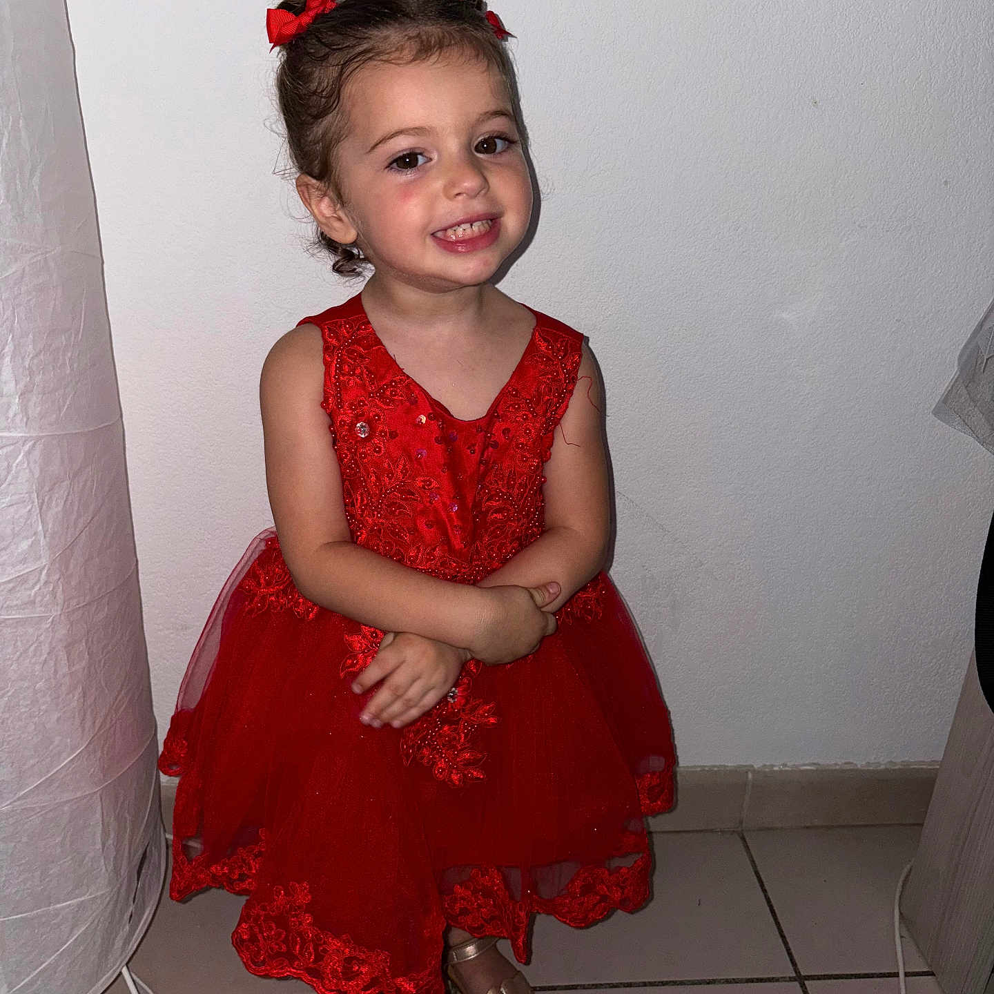 Alessya participe au concours pour gagner de l'argent avec cette photo : arms_crossed, child, cute, fashion, floor_lamp, footwear, girl, hair_bows, happy, indoor, person, portrait, red_dress, sandals, smiling, standing, tile_floor, toddler, wall, young_child