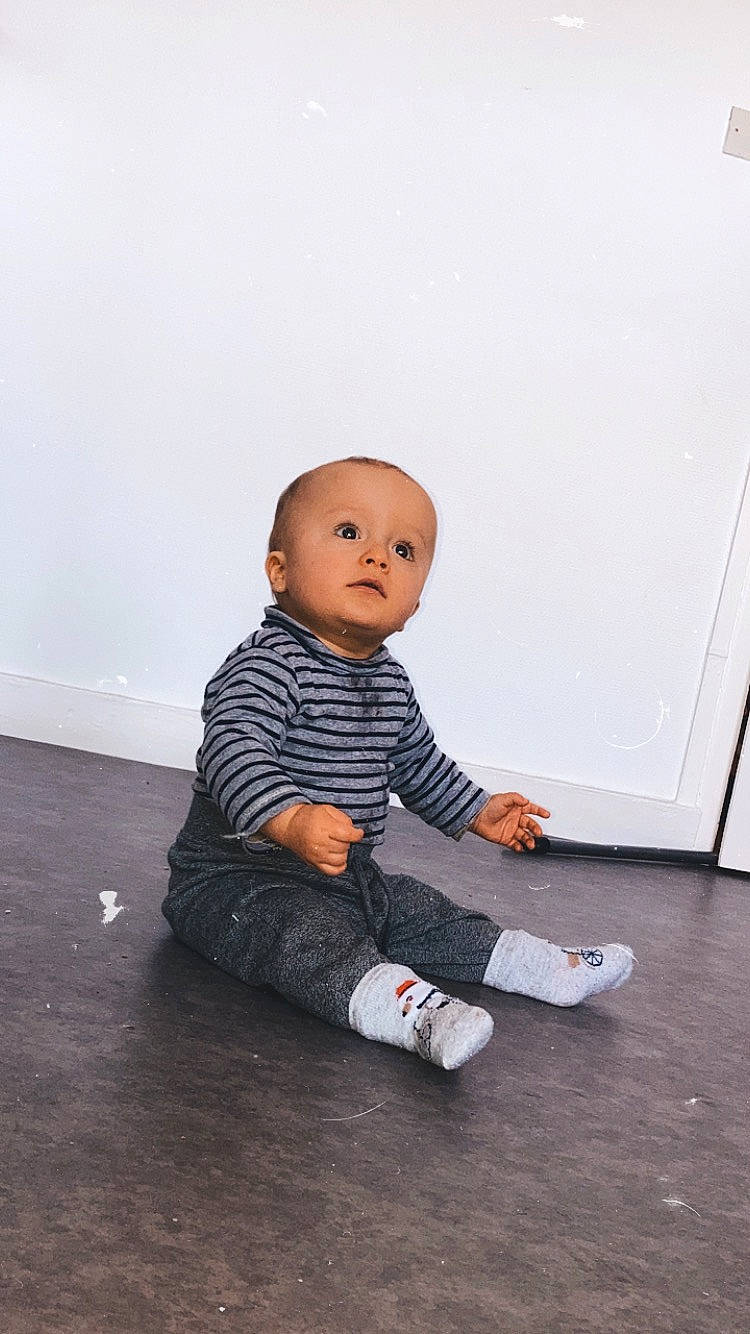Tylio participe au concours pour gagner de l'argent avec cette photo : baby, baby_toddler_clothing, cheek, child, flash_photography, floor, flooring, foot, fun, hairstyle, happy, hardwood, human_leg, knee, person, sitting, sleeve, t_shirt, toddler, wood