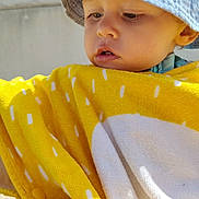 Lorenzo participe au concours pour gagner de l'argent avec cette photo : toddler, child, yellow_towel, bucket_hat, outdoor, sunlight, face, curious, young_child, summer, skin, headwear, closeup, blanket, daylight, portrait, baby, expression, casual, clothing