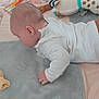 baby, infant, toy, blanket, plush_toy, bed, crib, sleepwear, child, tummy_time, soft_texture, cute, indoors, person, young_child, cozy, stuffed_animal, white_clothing, brown_pants, nursery