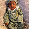 baby, child, knitwear, green_outfit, hat, bow_tie, blanket, star_pattern, infant, cute, portrait, sitting, cozy, soft_texture, hand, feet, sleepwear, indoors, young_child, face