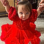 toddler, child, red_dress, sequins, ruffles, indoor, holding_hands, curious_expression, number_tag, event, floor, plaid_shirt, adult_hands, portrait, cute, person, young_child, looking_up, fashion, casual