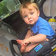 Josh is registered to the contest to win money with this photo: baby, child, car_seat, vehicle, portrait, blue_shirt, blond_hair, blue_eyes, sitting, indoors, backseat, infant, barefoot, toes, looking_at_camera, candid, car_interior, safety_straps, daylight, smiling