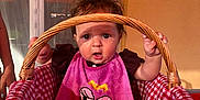 Lisa participe au concours pour gagner de l'argent avec cette photo : baby, basket, wicker, checkered_fabric, pink_bib, curious, indoor, child, holding, handle, wide_eyes, expression, hair, sunlight, shadow, mouth_open, seated, person, cute, portrait
